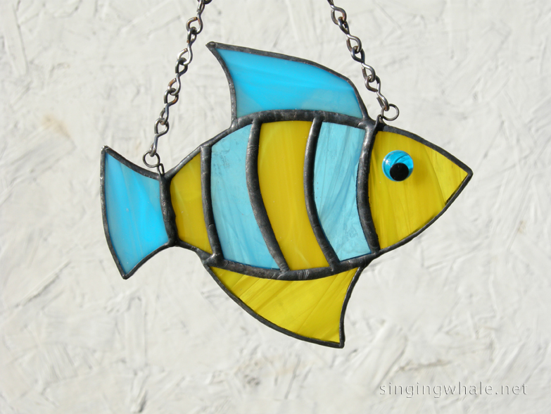 Made of light blue wispy and yellow wispy glass. Eye is a light blue wiggle eye securely glued on. Finished in a pewter patina. Measures 4 3/4 " wide by 4" tall. Fish in this pattern are $15 each.