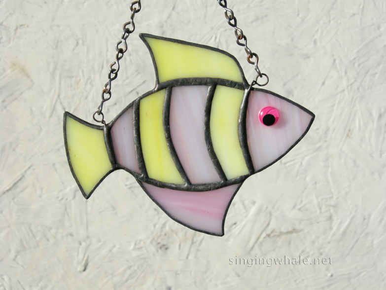 Made of translucent yellow and pink wispy glass. Eye is a pink wiggle eye securely glued on. Finished in a pewter patina. Measures 4 3/4 " wide by 4" tall. Fish in this pattern are $15 each.