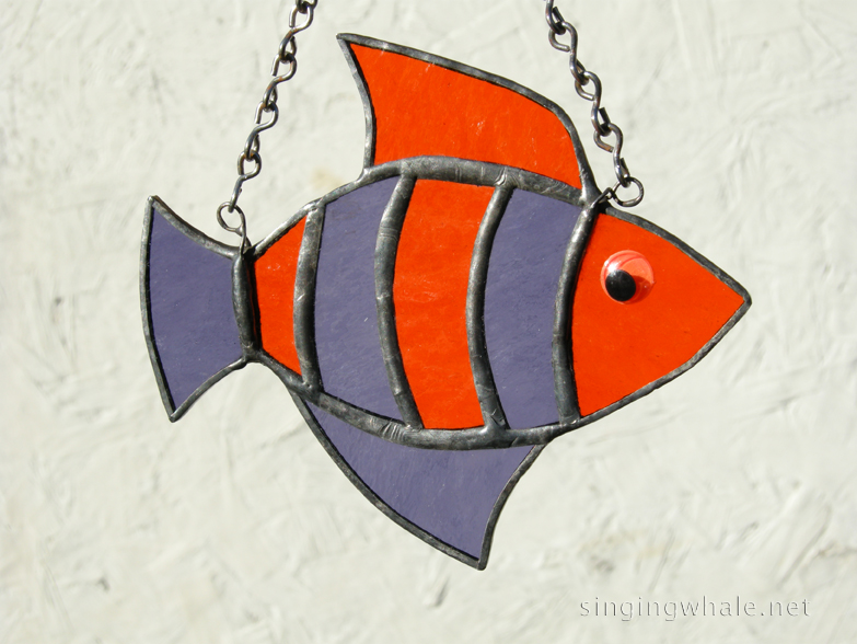 Made of purple and orange rough roll glass. Eye is an orange wiggle eye securely glued on. Finished in a pewter patina. Measures 4 3/4 " wide by 4" tall. Fish in this pattern are $15 each.