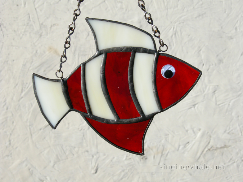 Made of translucent white and deep red glass. Eye is a white wiggle eye securely glued on. Finished in a pewter patina. Measures 4 3/4 " wide by 4" tall. Fish in this pattern are $15 each.