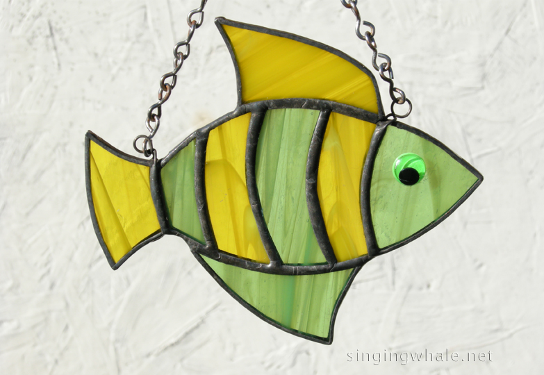 Made of light green wispy and yellow wispy glass. Eye is a bright green wiggle eye securely glued on. Finished in a pewter patina. Measures 4 3/4 " wide by 4" tall. Fish in this pattern are $15 each.